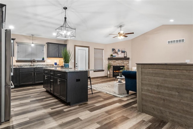 kitchen with a stone fireplace, light stone countertops, decorative light fixtures, a kitchen island, and a breakfast bar area