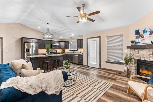 living room with a stone fireplace, ceiling fan, lofted ceiling, and hardwood / wood-style flooring