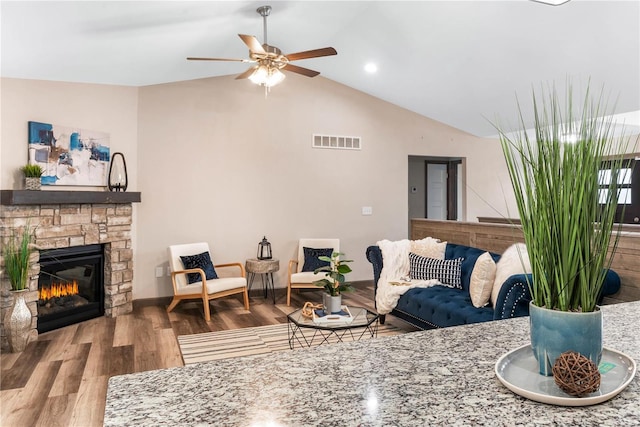 living room with a stone fireplace, ceiling fan, wood-type flooring, and vaulted ceiling