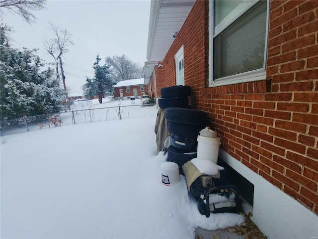 view of snow covered exterior with fence and brick siding