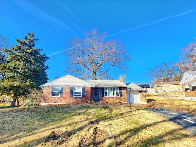 single story home featuring a garage, a front lawn, a chimney, and brick siding