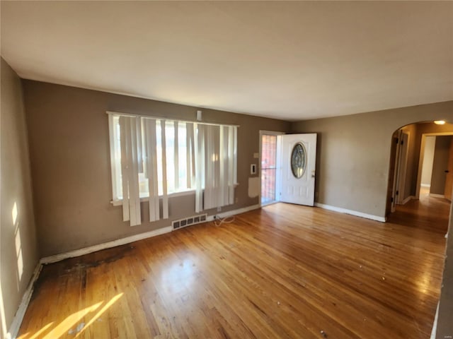 empty room featuring arched walkways, visible vents, baseboards, and wood finished floors