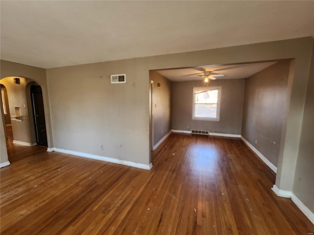 unfurnished room with ceiling fan, visible vents, arched walkways, and dark wood finished floors