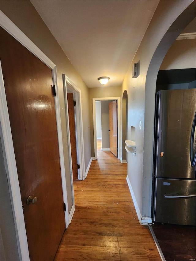 hallway featuring arched walkways, wood finished floors, and baseboards