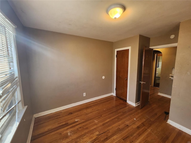 unfurnished bedroom featuring a closet, arched walkways, dark wood-style flooring, and baseboards