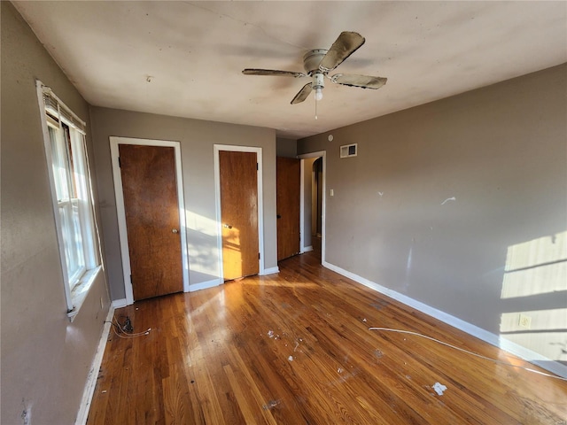 unfurnished bedroom with baseboards, visible vents, ceiling fan, wood finished floors, and multiple closets