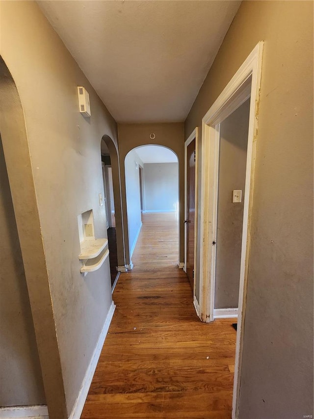 hall with baseboards, arched walkways, and wood finished floors