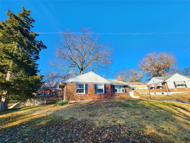 view of front of home featuring brick siding, a front lawn, a chimney, and fence