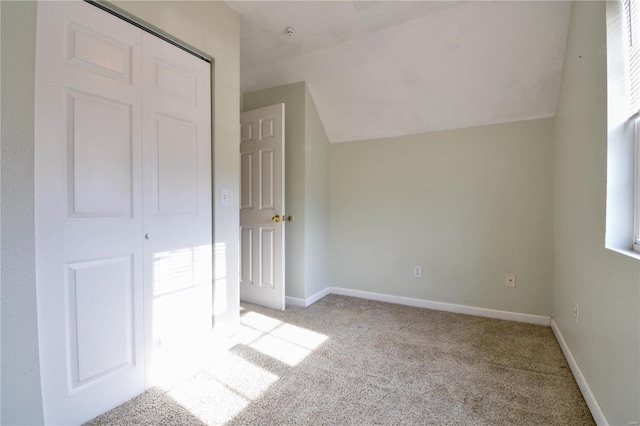 unfurnished bedroom with light carpet, a closet, multiple windows, and lofted ceiling