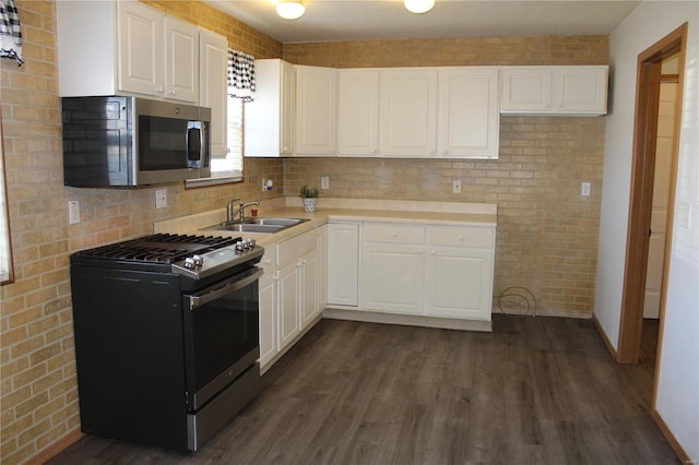 kitchen featuring sink, dark hardwood / wood-style floors, appliances with stainless steel finishes, white cabinetry, and brick wall