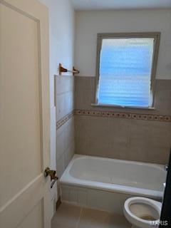 bathroom featuring tile patterned floors, a bath, toilet, and tile walls