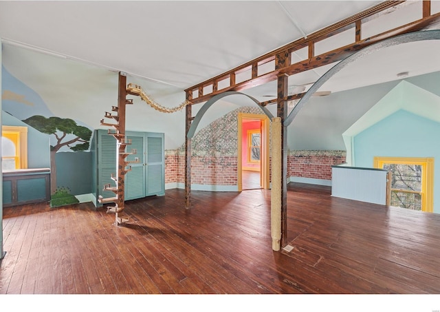 interior space featuring brick wall, wood-type flooring, and high vaulted ceiling