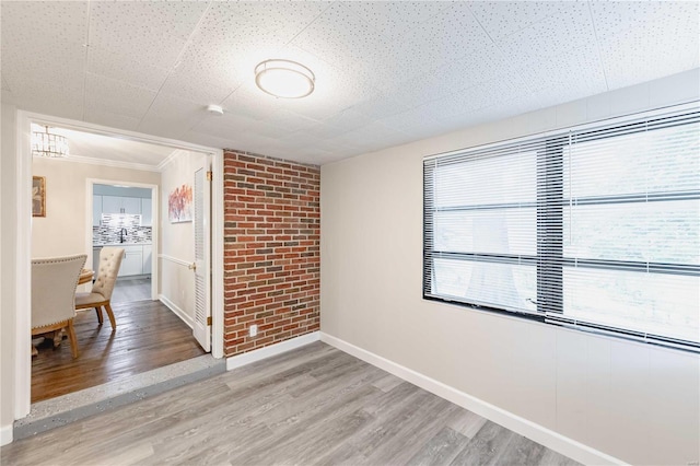 empty room featuring wood-type flooring, crown molding, and brick wall