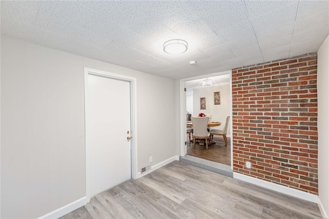 unfurnished room featuring brick wall and light hardwood / wood-style flooring