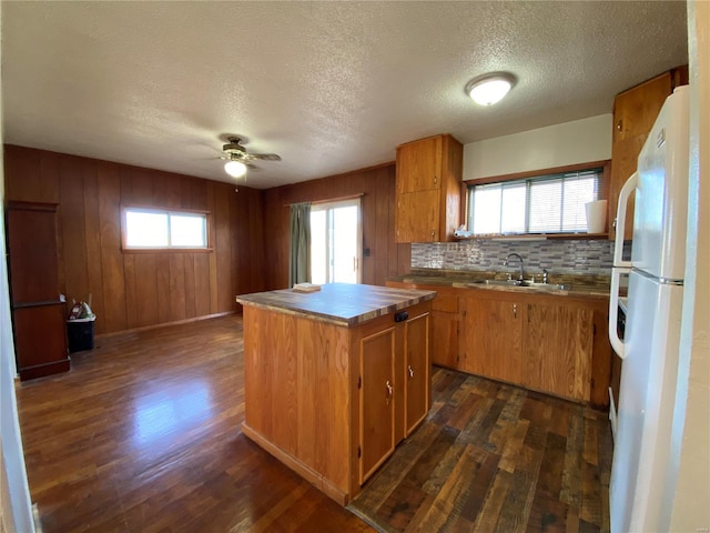 kitchen with white fridge, a kitchen island, dark wood-type flooring, and wood walls