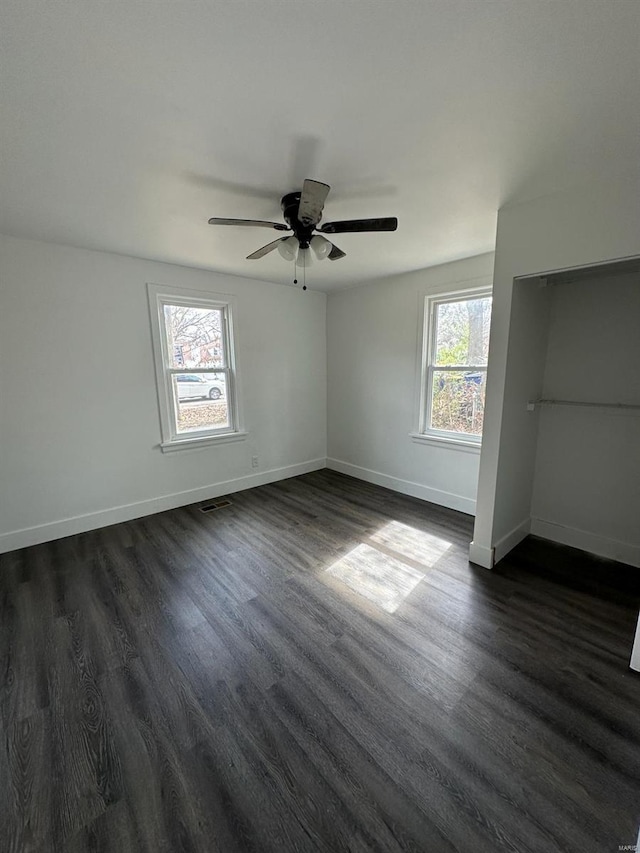 empty room with plenty of natural light, ceiling fan, and dark hardwood / wood-style flooring