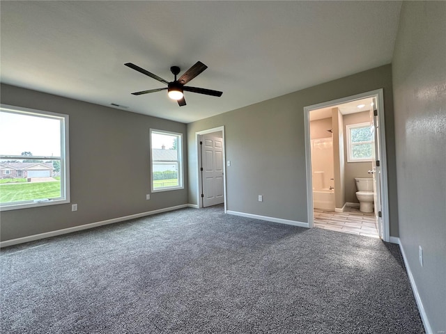 unfurnished bedroom featuring carpet flooring, multiple windows, ceiling fan, and connected bathroom