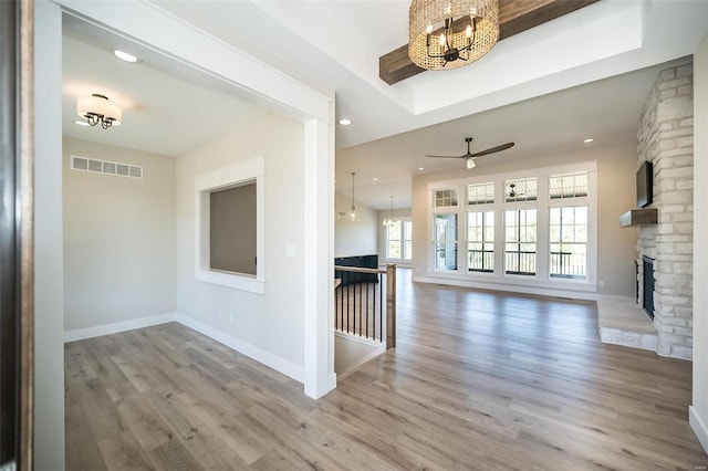 unfurnished living room featuring ceiling fan with notable chandelier, light hardwood / wood-style flooring, and a stone fireplace