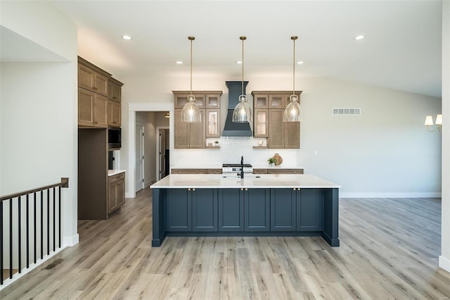 kitchen with lofted ceiling, a kitchen island with sink, sink, hanging light fixtures, and light hardwood / wood-style floors