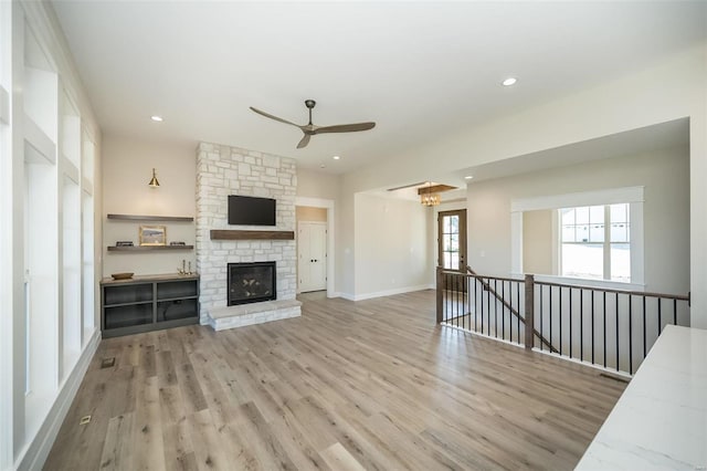 unfurnished living room with a stone fireplace, light hardwood / wood-style floors, and ceiling fan with notable chandelier