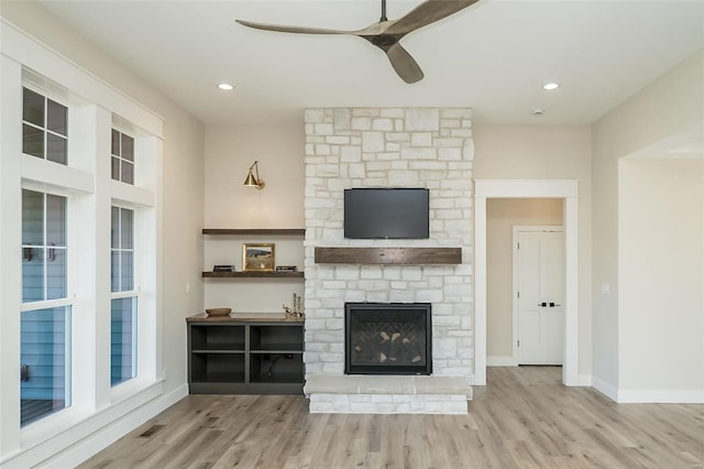 unfurnished living room featuring a stone fireplace, ceiling fan, and light hardwood / wood-style flooring