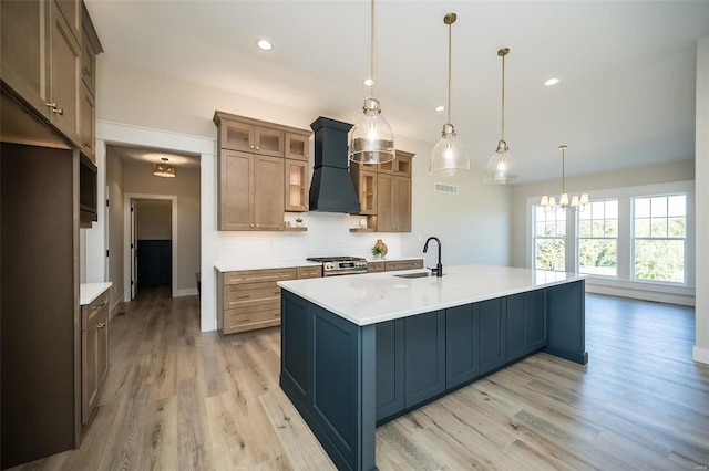 kitchen with sink, hanging light fixtures, backsplash, a center island with sink, and custom range hood