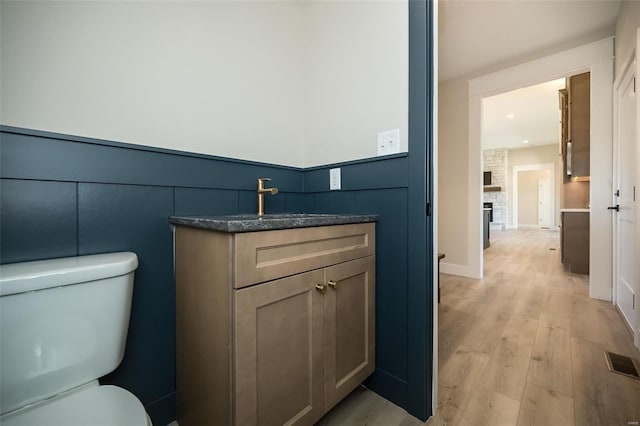 bathroom featuring wood-type flooring, vanity, toilet, and a stone fireplace