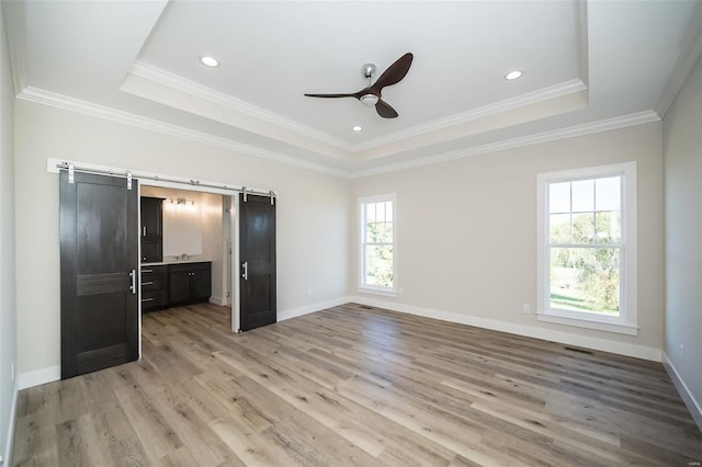 unfurnished bedroom with a raised ceiling, a barn door, crown molding, and multiple windows