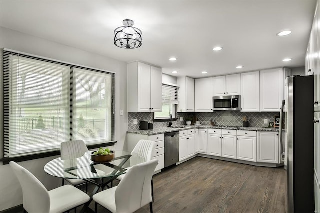 kitchen with backsplash, dark hardwood / wood-style floors, light stone countertops, appliances with stainless steel finishes, and white cabinetry