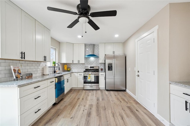 kitchen with light wood-type flooring, light stone counters, stainless steel appliances, wall chimney range hood, and white cabinets