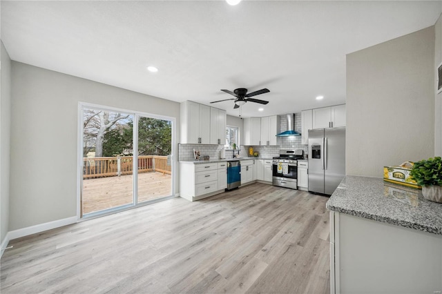 kitchen featuring light stone countertops, stainless steel appliances, white cabinetry, and wall chimney exhaust hood