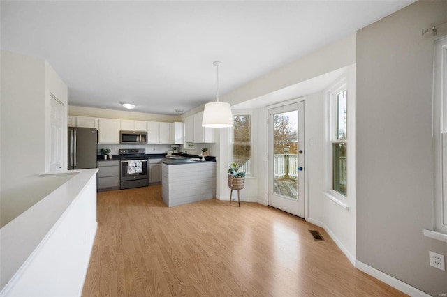 kitchen featuring hanging light fixtures, white cabinets, stainless steel appliances, and light hardwood / wood-style flooring