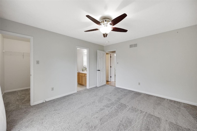 unfurnished bedroom with ensuite bathroom, ceiling fan, a spacious closet, light colored carpet, and a closet