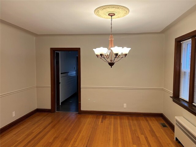 unfurnished room featuring a chandelier, wood-type flooring, and radiator