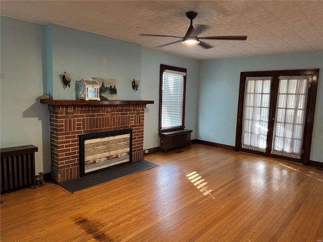 living room with radiator heating unit, hardwood / wood-style flooring, a brick fireplace, and ceiling fan