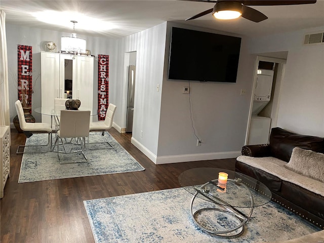 living room with stacked washer / drying machine, dark hardwood / wood-style flooring, and ceiling fan with notable chandelier