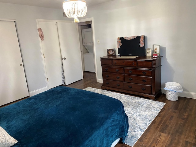 bedroom featuring stacked washer / dryer, dark wood-type flooring, and a notable chandelier