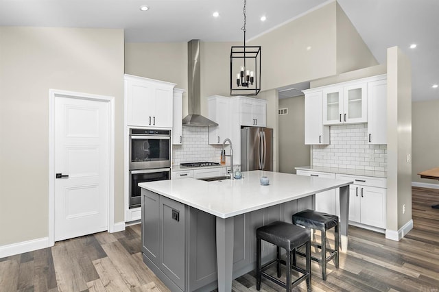 kitchen featuring white cabinets, an island with sink, wall chimney exhaust hood, and appliances with stainless steel finishes