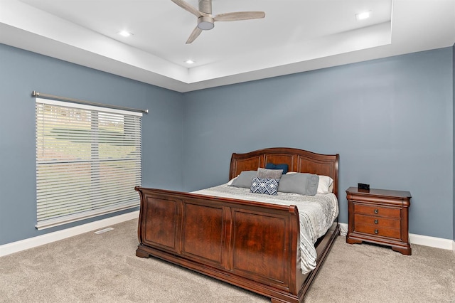 carpeted bedroom featuring a tray ceiling and ceiling fan