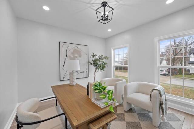 office with light wood-type flooring, an inviting chandelier, and a healthy amount of sunlight