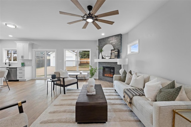 living room featuring a fireplace, light wood-type flooring, ceiling fan, and sink