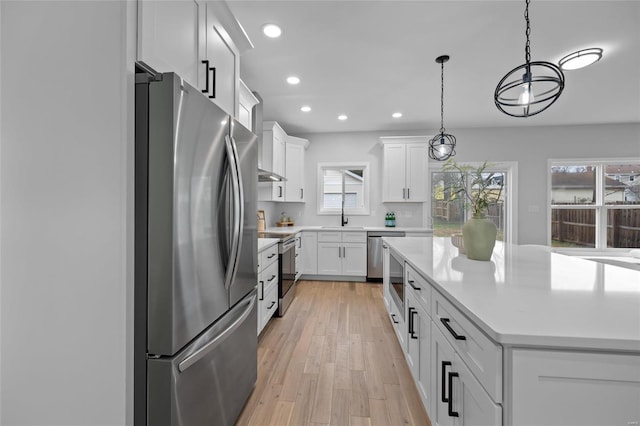 kitchen with white cabinetry, light wood-type flooring, decorative light fixtures, and appliances with stainless steel finishes