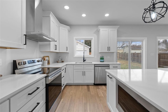 kitchen featuring pendant lighting, wall chimney exhaust hood, a healthy amount of sunlight, and appliances with stainless steel finishes