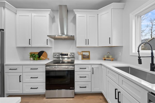 kitchen with white cabinetry, sink, wall chimney range hood, light hardwood / wood-style floors, and appliances with stainless steel finishes