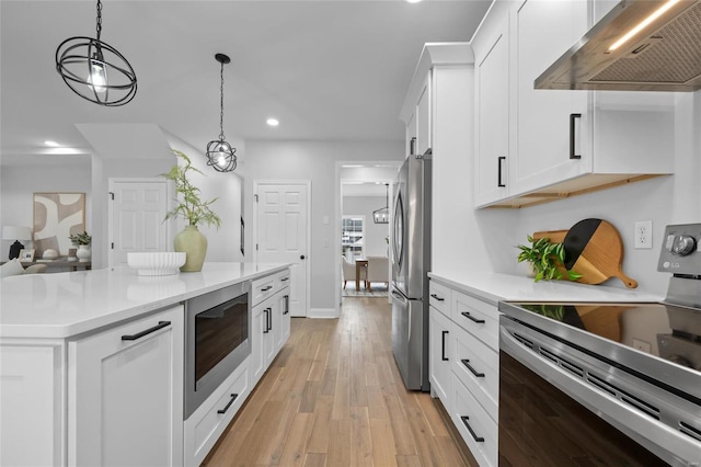 kitchen with exhaust hood, white cabinets, appliances with stainless steel finishes, decorative light fixtures, and light hardwood / wood-style floors