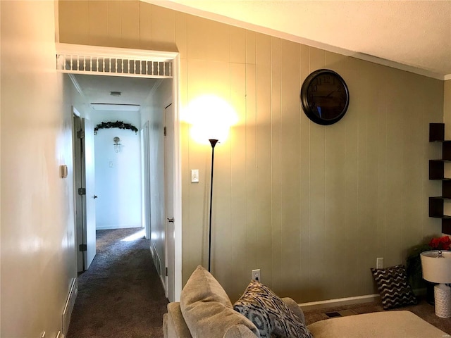 hallway featuring crown molding, a textured ceiling, lofted ceiling, wooden walls, and dark carpet