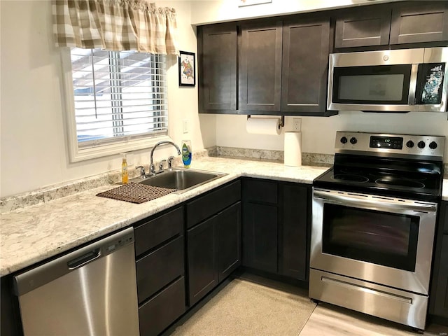 kitchen featuring light stone countertops, sink, light hardwood / wood-style floors, dark brown cabinets, and appliances with stainless steel finishes