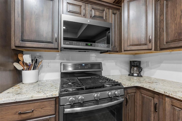 kitchen featuring dark brown cabinets, backsplash, stainless steel appliances, and light stone counters