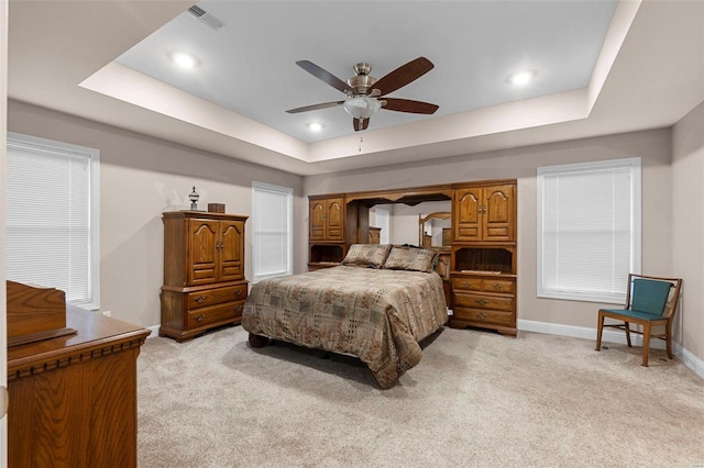 bedroom with ceiling fan, light colored carpet, and a tray ceiling