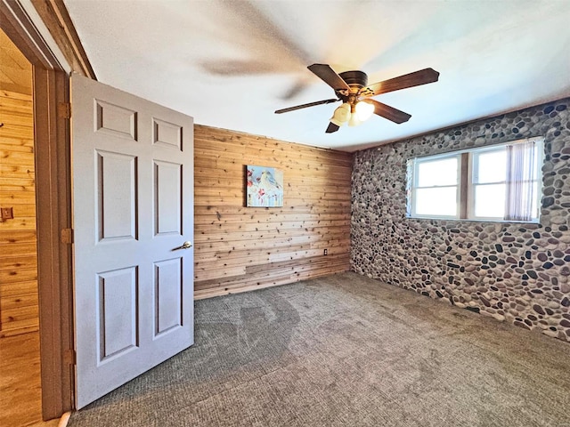 unfurnished bedroom with ceiling fan, wooden walls, and dark carpet